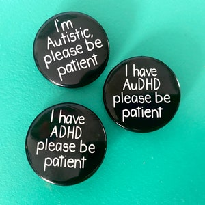 Può includere: Tre badge a bottone neri con testo bianco. Il primo badge dice "Sono autistico, per favore sii paziente". Il secondo badge dice "Ho ADHD, per favore sii paziente". Il terzo badge dice "Ho AuDHD, per favore sii paziente".