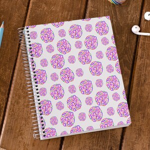 Puede incluir: Una libreta de espiral blanca con un patr&oacute;n de cerebro rosa, azul y verde.