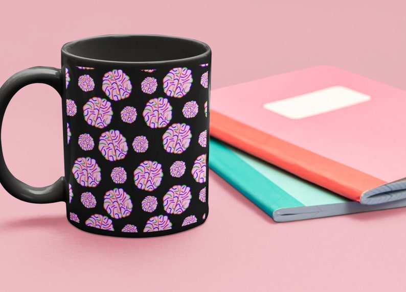 Puede incluir: Una taza de caf&eacute; negra con un patr&oacute;n de formas de cerebro rosas y moradas sobre un fondo negro.