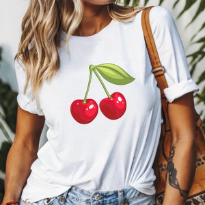 May include: White t-shirt featuring a cartoon illustration of two bright red cherries with a green leaf. The cherries have a glossy finish and are connected by a green stem. The shirt is a casual style.
