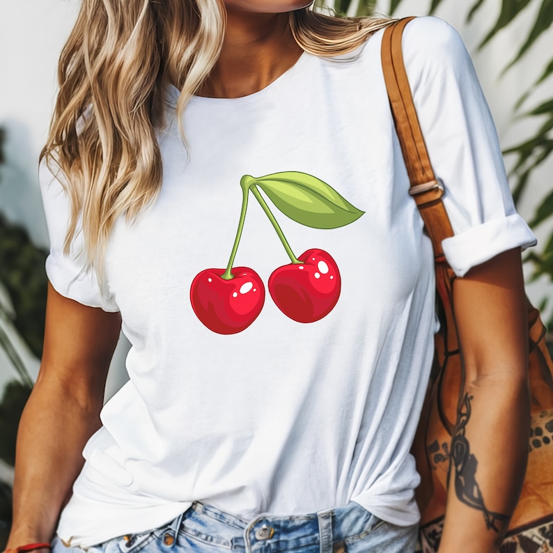 May include: White t-shirt featuring a cartoon illustration of two bright red cherries with a green leaf. The cherries have a glossy finish and are connected by a green stem. The shirt is a casual style.