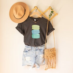 May include: A dark gray V-neck t-shirt with a stack of three pastel green, blue, and teal macarons on the front.