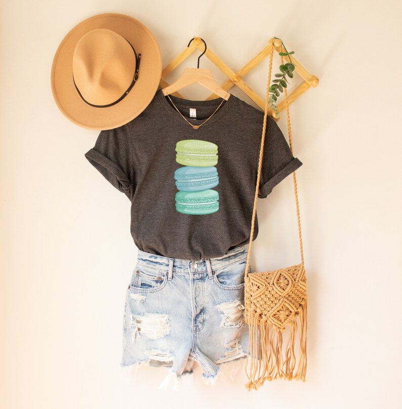 May include: A dark gray V-neck t-shirt with a stack of three pastel green, blue, and teal macarons on the front.