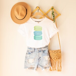 May include: A white t-shirt with a stack of three pastel green and blue macarons on the front.