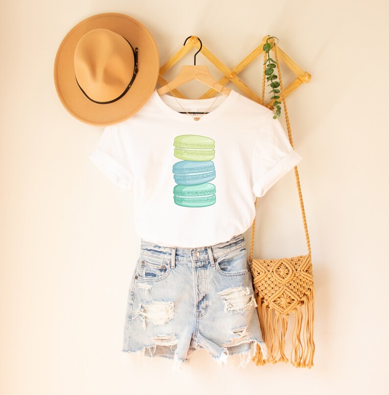 May include: A white t-shirt with a stack of three pastel green and blue macarons on the front.