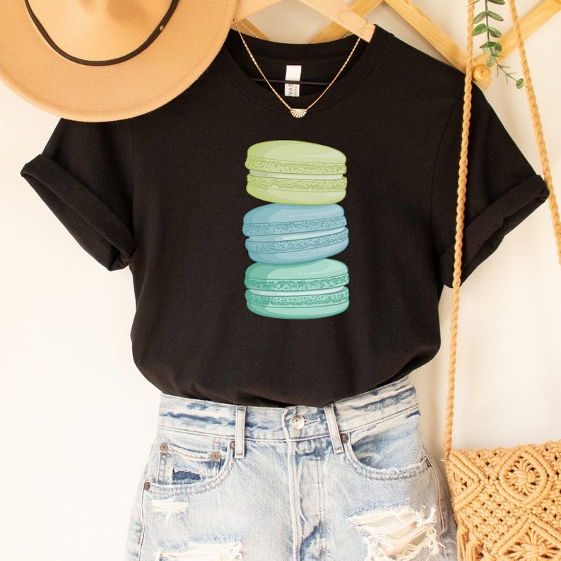 May include: A black t-shirt with a stack of three pastel green and blue macarons printed on the front.