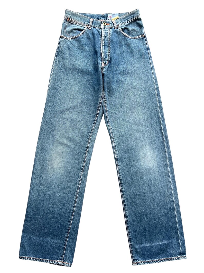 May include: Light blue denim jeans with a classic five-pocket design. The jeans have a button and zipper closure, belt loops, and a straight leg fit. The denim has a faded wash and subtle wear marks.