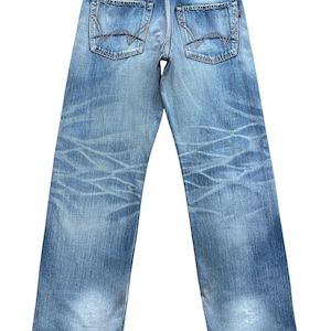 Pu&ograve; includere: Jeans in denim blu chiaro con lavaggio sbiadito e dettagli usurati. Presenta tasche posteriori con cuciture decorative e un'etichetta in pelle con il marchio "EDWIN". I jeans hanno un taglio dritto.