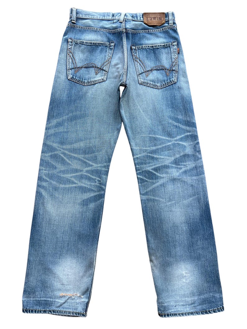 Pu&ograve; includere: Jeans in denim blu chiaro con lavaggio sbiadito e dettagli usurati. Presenta tasche posteriori con cuciture decorative e un'etichetta in pelle con il marchio "EDWIN". I jeans hanno un taglio dritto.