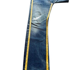 Pu&ograve; includere: Jeans blu in denim dall'aspetto vissuto, con ginocchio strappato e sbiaditura. Un metro a nastro giallo &egrave; posizionato lungo i jeans. I jeans misurano circa 102 cm di lunghezza.