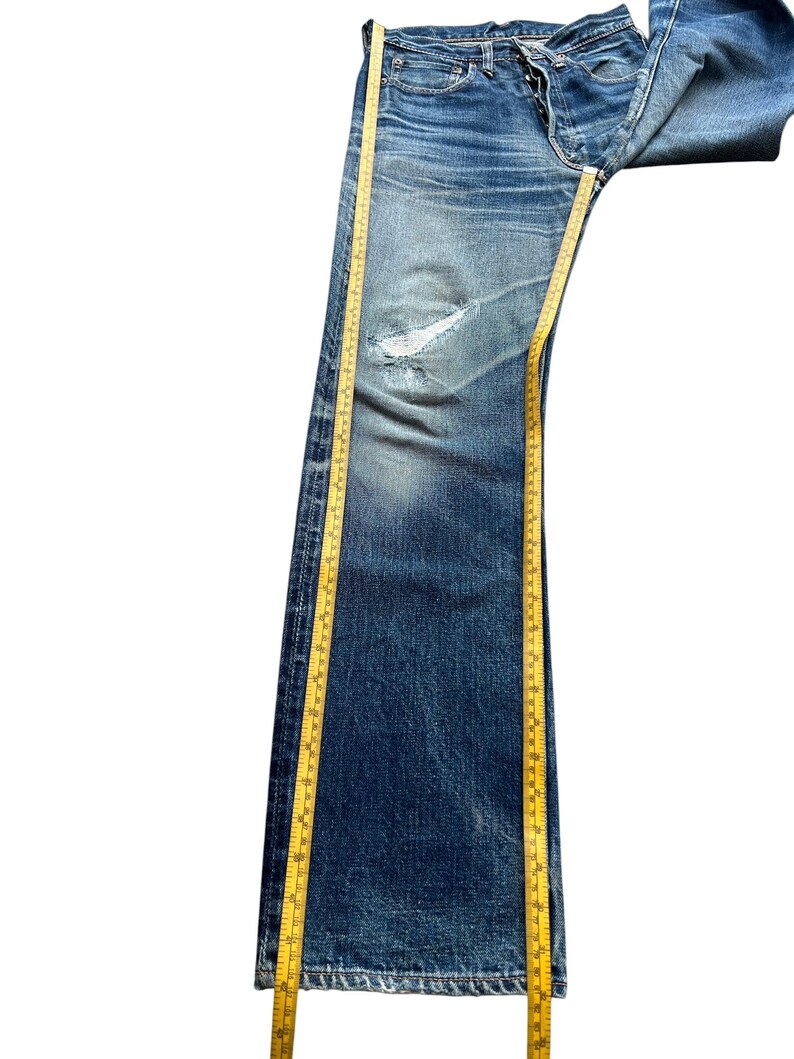 Pu&ograve; includere: Jeans blu in denim dall'aspetto vissuto, con ginocchio strappato e sbiaditura. Un metro a nastro giallo &egrave; posizionato lungo i jeans. I jeans misurano circa 102 cm di lunghezza.