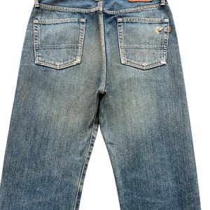 May include: Faded blue denim jeans with two back pockets and a leather patch. The jeans have a classic five-pocket design and a straight leg fit. The denim has a worn, distressed look.
