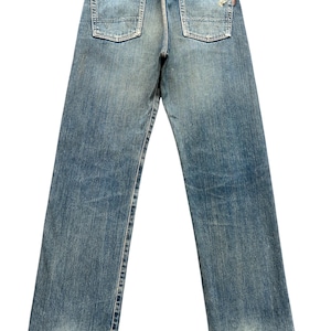 May include: Faded blue denim jeans with a classic five-pocket design. The jeans show signs of wear, including distressed areas at the hem and fading throughout. A brown leather patch is visible at the back waistband.