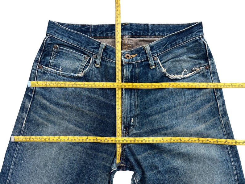 Puede incluir: Primer plano de unos vaqueros azules con una cinta m&eacute;trica amarilla colocada sobre la cintura y las piernas. Los vaqueros tienen un dise&ntilde;o cl&aacute;sico de cinco bolsillos y muestran signos de desgaste. La cinta m&eacute;trica est&aacute; en cent&iacute;metros.