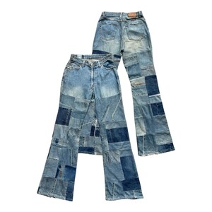 Può includere: Due paia di jeans in denim patchwork. I jeans sono blu chiaro con toppe blu scuro cucite. Un paio è steso piatto, l'altro è leggermente angolato, mostrando il design e la consistenza del tessuto.