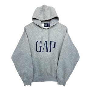 May include: A gray hooded sweatshirt with the word "GAP" embroidered in navy blue across the chest. The sweatshirt has a drawstring hood and a small tag with the "GAP" logo near the hood.