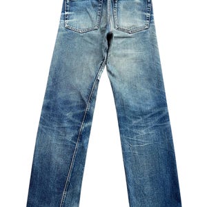 Pu&ograve; includere: Jeans in denim blu sbiadito con un classico design a cinque tasche. I jeans mostrano segni di usura, con aree rovinate e una toppa in pelle sul retro. Il taglio dritto e il lavaggio medio conferiscono un aspetto vintage.