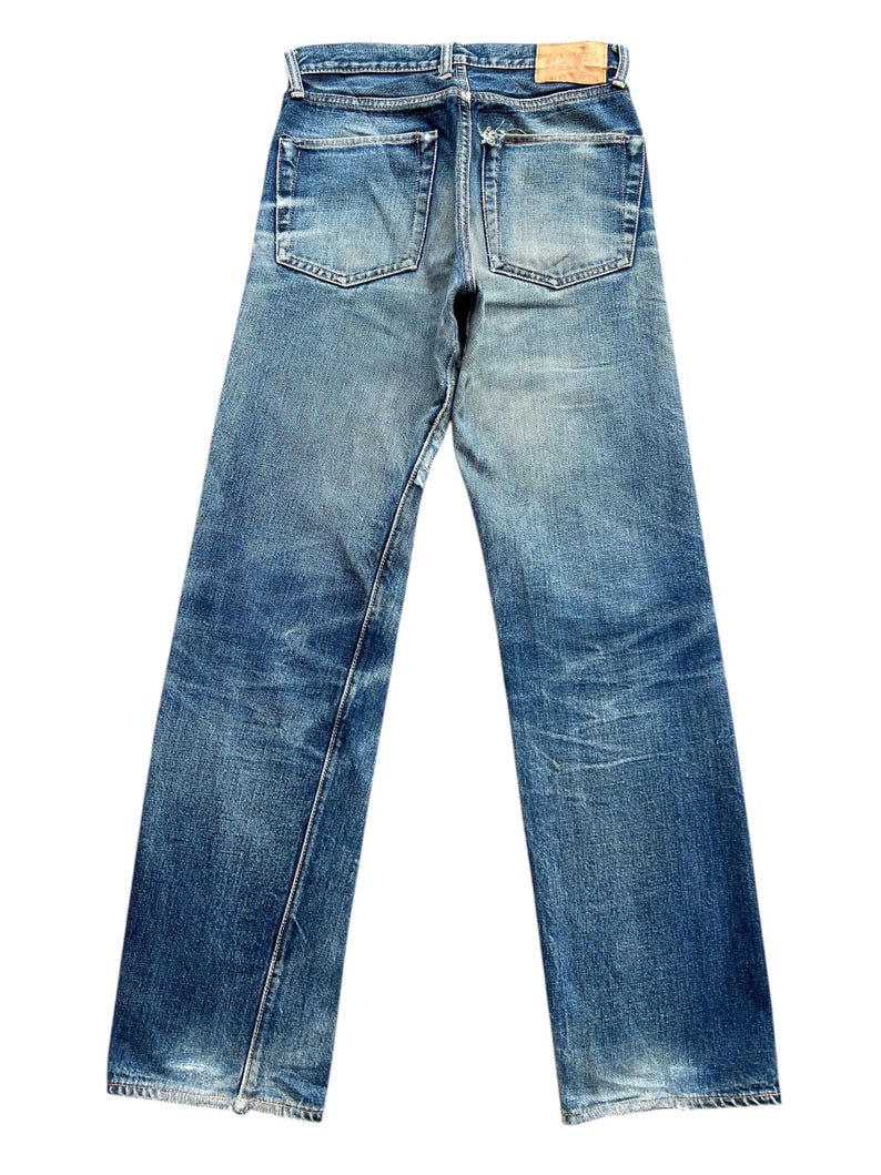 Pu&ograve; includere: Jeans in denim blu sbiadito con un classico design a cinque tasche. I jeans mostrano segni di usura, con aree rovinate e una toppa in pelle sul retro. Il taglio dritto e il lavaggio medio conferiscono un aspetto vintage.