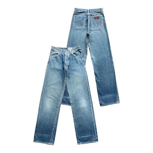May include: Two pairs of light blue denim jeans. One pair is laid flat, showing the front, while the other is angled, displaying the back pockets and a brown leather patch. The jeans have a classic, straight-leg fit.