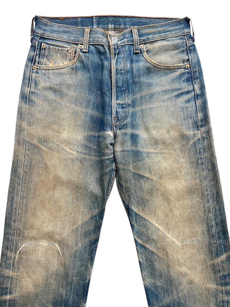 May include: Faded blue denim jeans with a button fly and classic five-pocket design. The jeans show signs of wear and tear, with faded patches and distressed areas. The jeans have a straight leg cut and a medium rise.