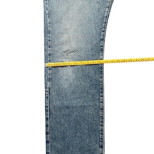 K&ouml;nnte beinhalten: Hellblaue Jeans mit gelbem Ma&szlig;band auf dem Kleidungsst&uuml;ck. Die Jeans hat eine mittlere Waschung mit sichtbaren Gebrauchsspuren. Das Ma&szlig;band wird verwendet, um die L&auml;nge und Breite der Jeans zu messen.