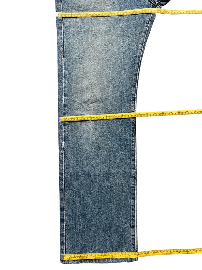 K&ouml;nnte beinhalten: Hellblaue Jeans mit gelbem Ma&szlig;band auf dem Kleidungsst&uuml;ck. Die Jeans hat eine mittlere Waschung mit sichtbaren Gebrauchsspuren. Das Ma&szlig;band wird verwendet, um die L&auml;nge und Breite der Jeans zu messen.
