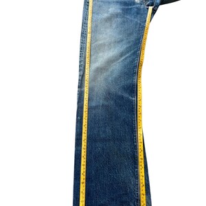 以下が含まれることがあります： ボタンフライの青いデニムジーンズ。黄色の巻尺で測定されています。ジーンズは使用感と色あせが見られます。巻尺はジーンズの長さを示しています。