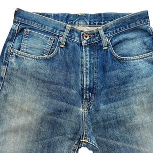 May include: Close-up of blue denim jeans. The jeans have a button closure, front pockets, and belt loops. The denim has a faded, worn appearance.