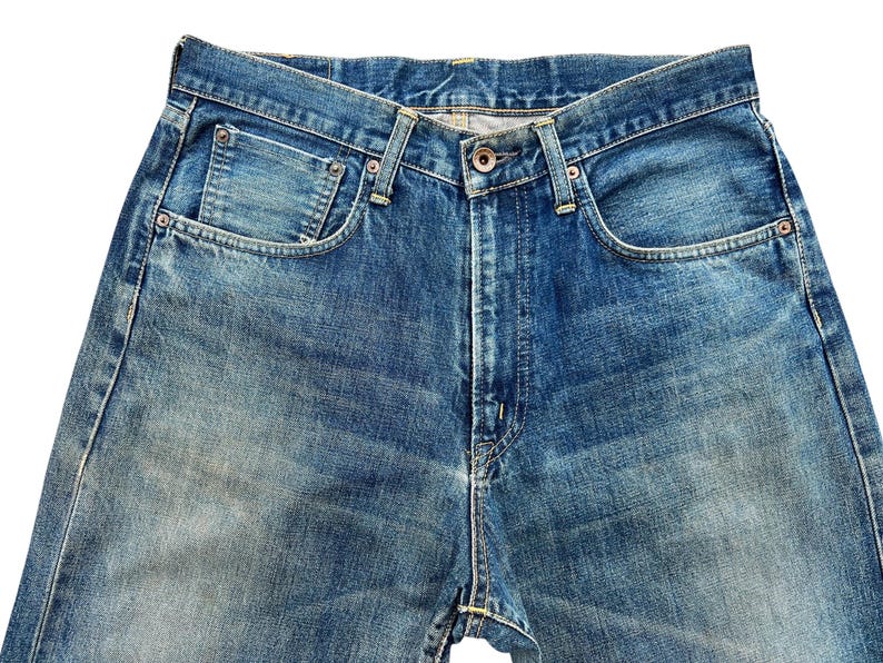 May include: Close-up of blue denim jeans. The jeans have a button closure, front pockets, and belt loops. The denim has a faded, worn appearance.