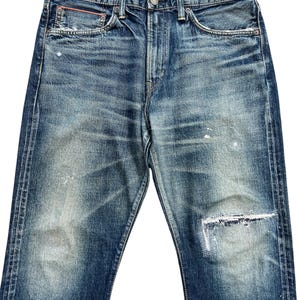 Puede incluir: Vaqueros de mezclilla azul descolorido con aspecto desgastado. Los vaqueros tienen cierre de bot&oacute;n, dise&ntilde;o cl&aacute;sico de cinco bolsillos y rodilla parcheada. La mezclilla tiene un aspecto desgastado con decoloraci&oacute;n clara y sutil desgaste.