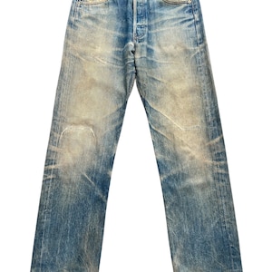 May include: Faded blue denim jeans with a button fly and classic five-pocket design. The jeans show signs of wear, with distressed areas and a light wash effect. The straight-leg cut and worn details give them a vintage aesthetic.