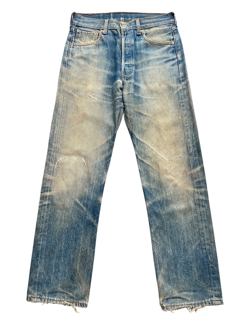May include: Faded blue denim jeans with a button fly and classic five-pocket design. The jeans show signs of wear, with distressed areas and a light wash effect. The straight-leg cut and worn details give them a vintage aesthetic.