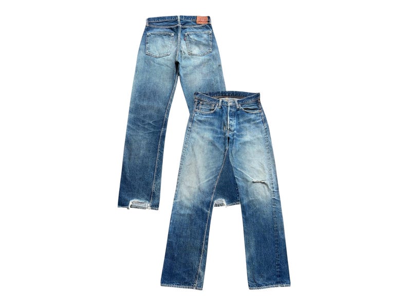 以下が含まれることがあります： ヴィンテージの青いデニムジーンズが2足。1足は後ろから表示され、ポケットとベルトループが見えます。もう1足は前から表示され、膝が破れていて、色あせたウォッシュ加工が施されています。どちらのペアもクラシックなストレートレッグフィットです。