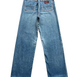 May include: Light blue denim jeans with a wide leg design. The jeans feature two back pockets with a stitched design and a brown leather patch. The jeans are a vintage style.