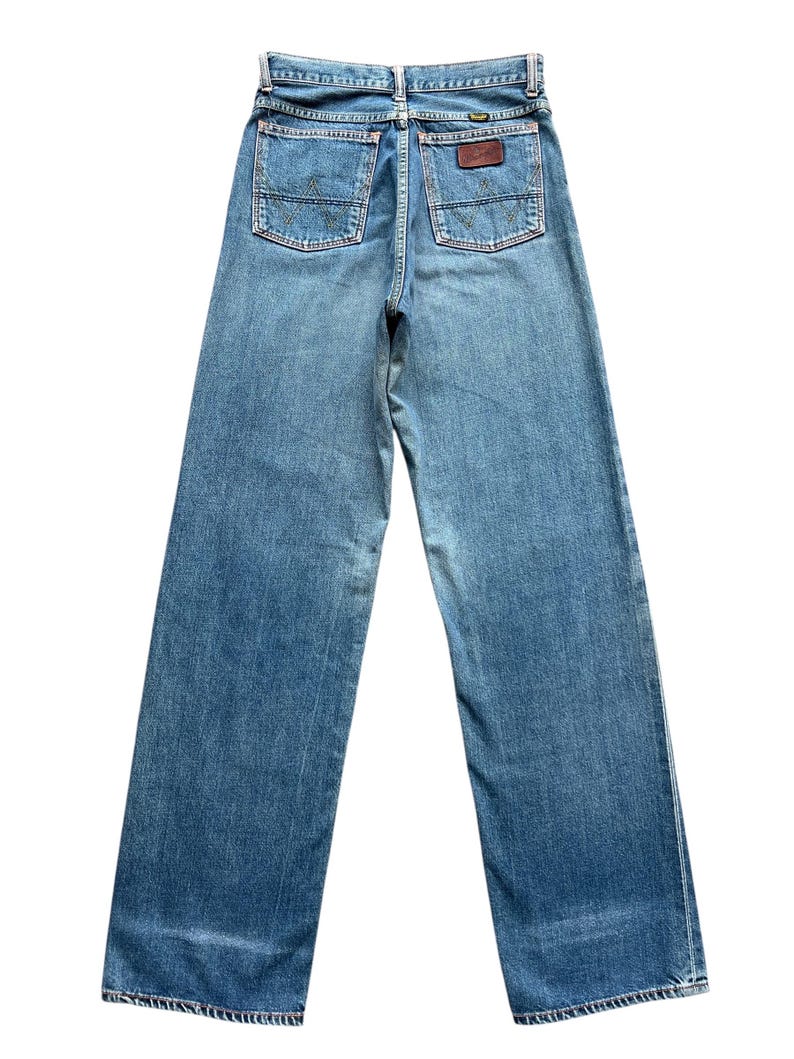 May include: Light blue denim jeans with a wide leg design. The jeans feature two back pockets with a stitched design and a brown leather patch. The jeans are a vintage style.