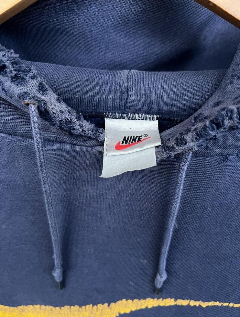 Puede incluir: Una sudadera con capucha azul marino con una etiqueta blanca de Nike en la parte delantera. La sudadera tiene un aspecto desgastado con bordes deshilachados alrededor de la capucha.
