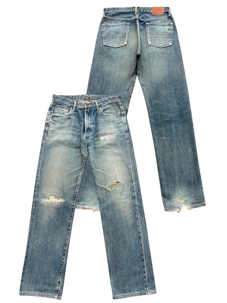 May include: Two pairs of light blue denim jeans with a faded wash and distressed details. One pair is laid flat, the other is upright, showing the back pockets and a leather patch. Both pairs have ripped knees and frayed hems.