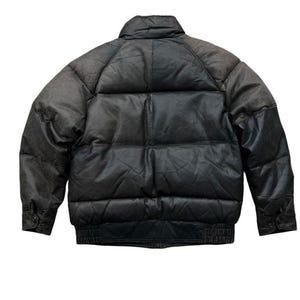 May include: A black leather puffer jacket with a high collar and ribbed cuffs. The jacket has a quilted design and a bomber-style fit. The leather appears worn, with a gradient from dark brown to black.