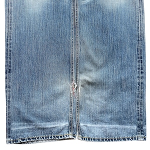 Pu&ograve; includere: Primo piano di un paio di jeans blu in denim. I jeans mostrano segni di usura e sbiadimento, con un'area usurata vicino al fondo. Le cuciture sono visibili lungo le cuciture e l'orlo. L'aspetto generale &egrave; casual e usurato.