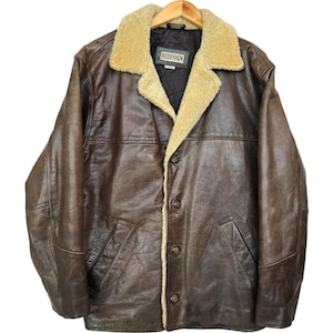 Könnte beinhalten: Braune Lederjacke mit beigem Lammfellkragen und Futter. Die Jacke hat eine Knopfleiste, zwei Vordertaschen und den Markennamen "HIDESIGN" auf einem Etikett innen. Sie hängt an einem Holzkleiderbügel.