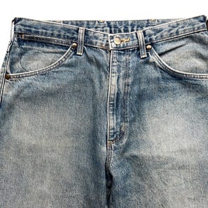 K&ouml;nnte beinhalten: Nahaufnahme einer hellblauen Jeans. Die Jeans hat ein klassisches F&uuml;nf-Taschen-Design mit Nieten an den Ecken der Vordertaschen. Der Denim hat ein verblasstes, abgenutztes Aussehen mit subtilen Farbvariationen.