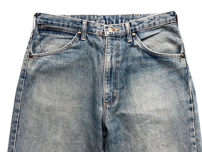 K&ouml;nnte beinhalten: Nahaufnahme einer hellblauen Jeans. Die Jeans hat ein klassisches F&uuml;nf-Taschen-Design mit Nieten an den Ecken der Vordertaschen. Der Denim hat ein verblasstes, abgenutztes Aussehen mit subtilen Farbvariationen.