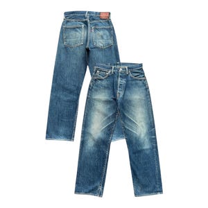 Puede incluir: Dos pares de pantalones vaqueros de mezclilla azul, un par está doblado y colocado encima del otro. Ambos pares tienen un aspecto descolorido y están desgastados.