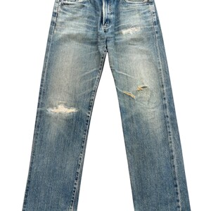 May include: Light blue denim jeans with distressed details, including rips on the knees and thighs. The jeans have a classic five-pocket design, a button and zipper closure, and a faded wash for a vintage look. The jeans are straight-legged.