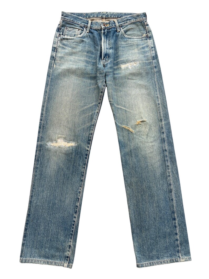 May include: Light blue denim jeans with distressed details, including rips on the knees and thighs. The jeans have a classic five-pocket design, a button and zipper closure, and a faded wash for a vintage look. The jeans are straight-legged.