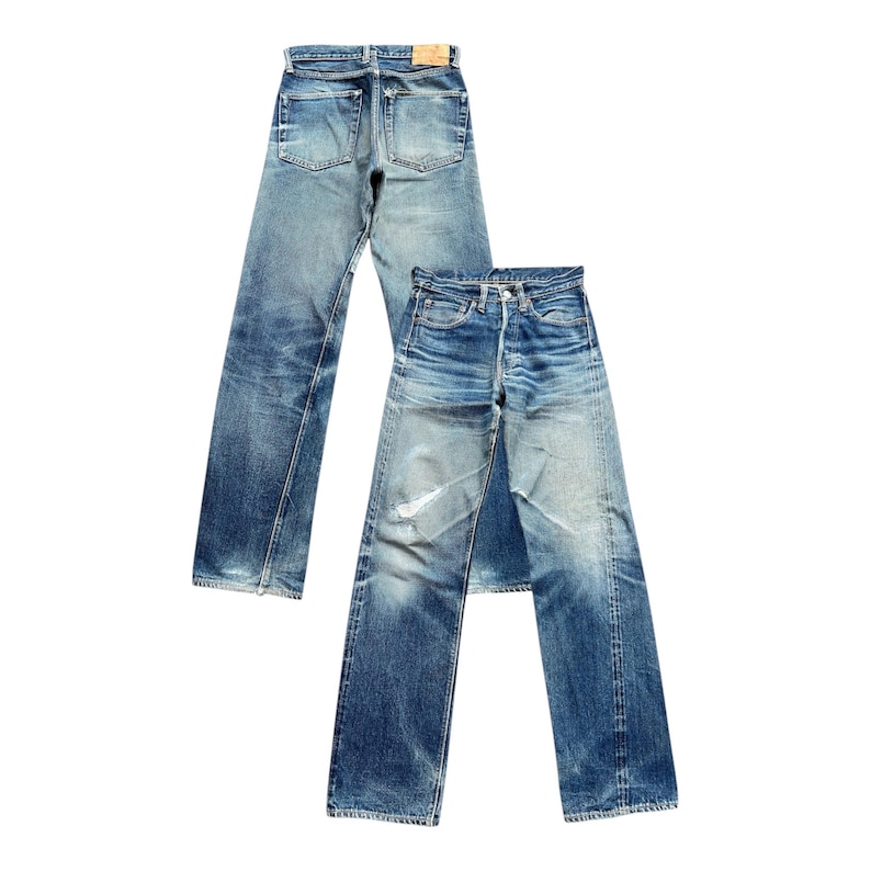 Pu&ograve; includere: Due paia di jeans in denim blu con un lavaggio sbiadito. Un paio &egrave; posizionato dietro l'altro, mostrando il retro e il davanti dei jeans. I jeans hanno un classico design a cinque tasche e una chiusura con bottoni.