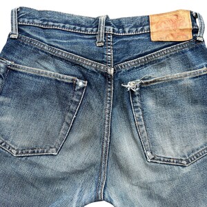Pu&ograve; includere: Primo piano del retro di jeans blu. I jeans hanno due tasche posteriori e una toppa in pelle. Il denim &egrave; sbiadito con qualche segno di usura intorno alle tasche e ai passanti.