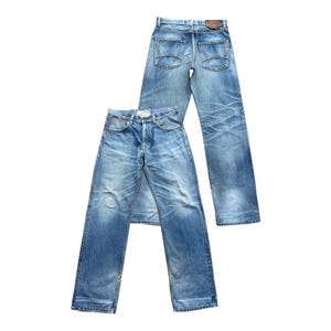 Pu&ograve; includere: Due paia di jeans in denim blu chiaro. Un paio &egrave; steso, l'altro &egrave; in piedi. Entrambi i paia hanno un lavaggio sbiadito, dettagli usurati e uno stile classico a cinque tasche. I jeans hanno una chiusura con bottoni e una toppa in pelle.