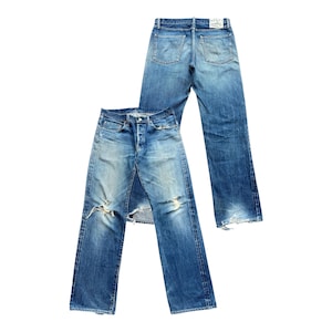May include: Two pairs of blue denim jeans. One pair is laid over the other. The top pair is a lighter wash with distressed details, including rips at the knees. The bottom pair is a darker wash with a classic five-pocket design.