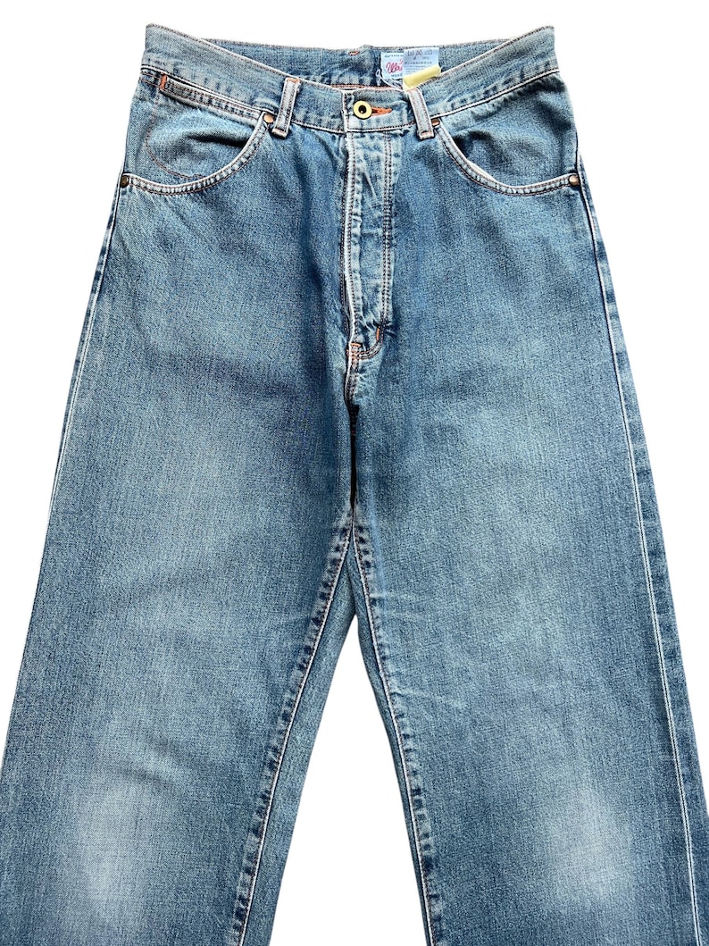 May include: Light blue denim jeans with a classic five-pocket design. The jeans feature a button and zipper closure, belt loops, and a faded wash for a vintage look. The stitching is visible in a contrasting color.